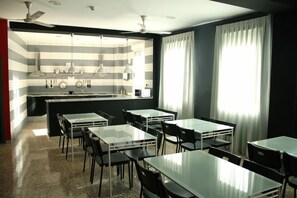 A modern kitchen with striped backsplash, a central island, and pendant lighting. There are tables and chairs arranged for dining.