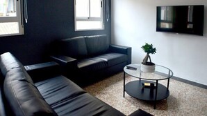 Una sala de estar moderna con un sofá de cuero negro, una mesa de centro de vidrio y una planta en maceta.
