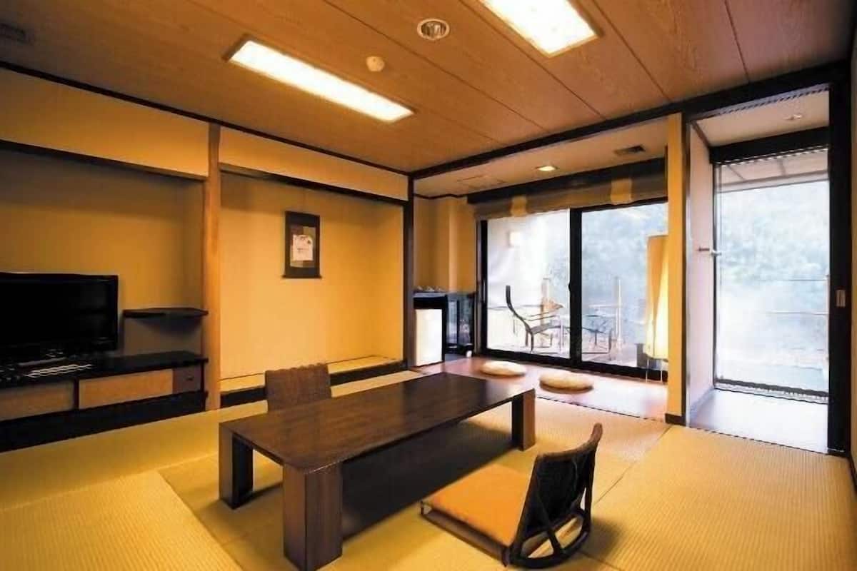 A room with a wooden ceiling, a television, a dining table with chairs, and large windows.