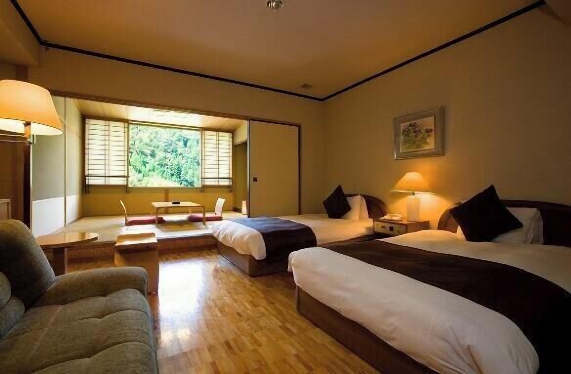Une chambre d’hôtel avec deux lits, un canapé, un bureau et une fenêtre donnant sur un espace verdoyant.