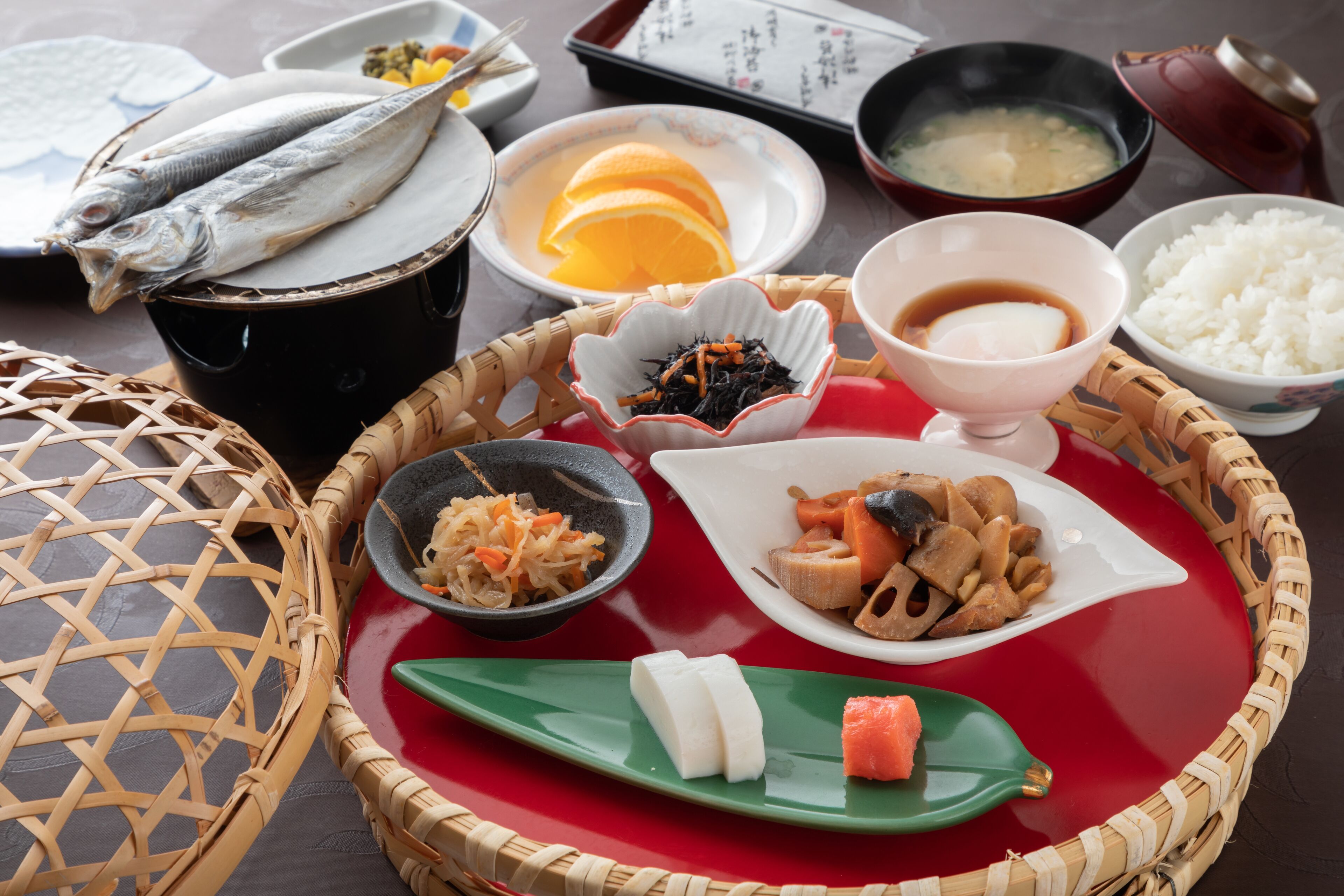 A traditional Japanese meal with fish, vegetables, and rice on a red tray.
