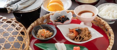 A traditional Japanese meal with fish, vegetables, and rice on a red tray.
