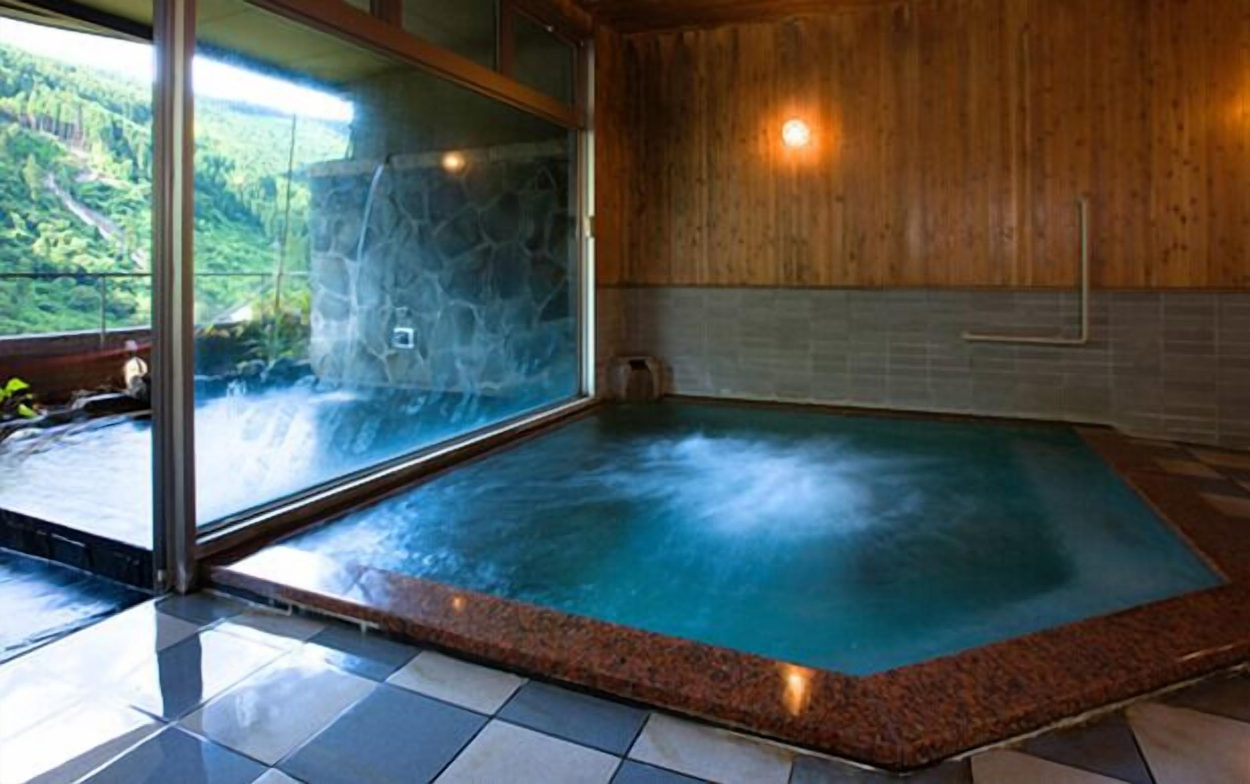 Un bain à remous avec un mur en pierre et un plancher en bois, une fenêtre donnant sur une forêt et un sol carrelé.