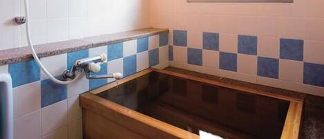 Ein Badezimmer mit einer Holzwanne, blau-weißen Schachbrettfliesen und einem Fenster mit Blick ins Grüne.
