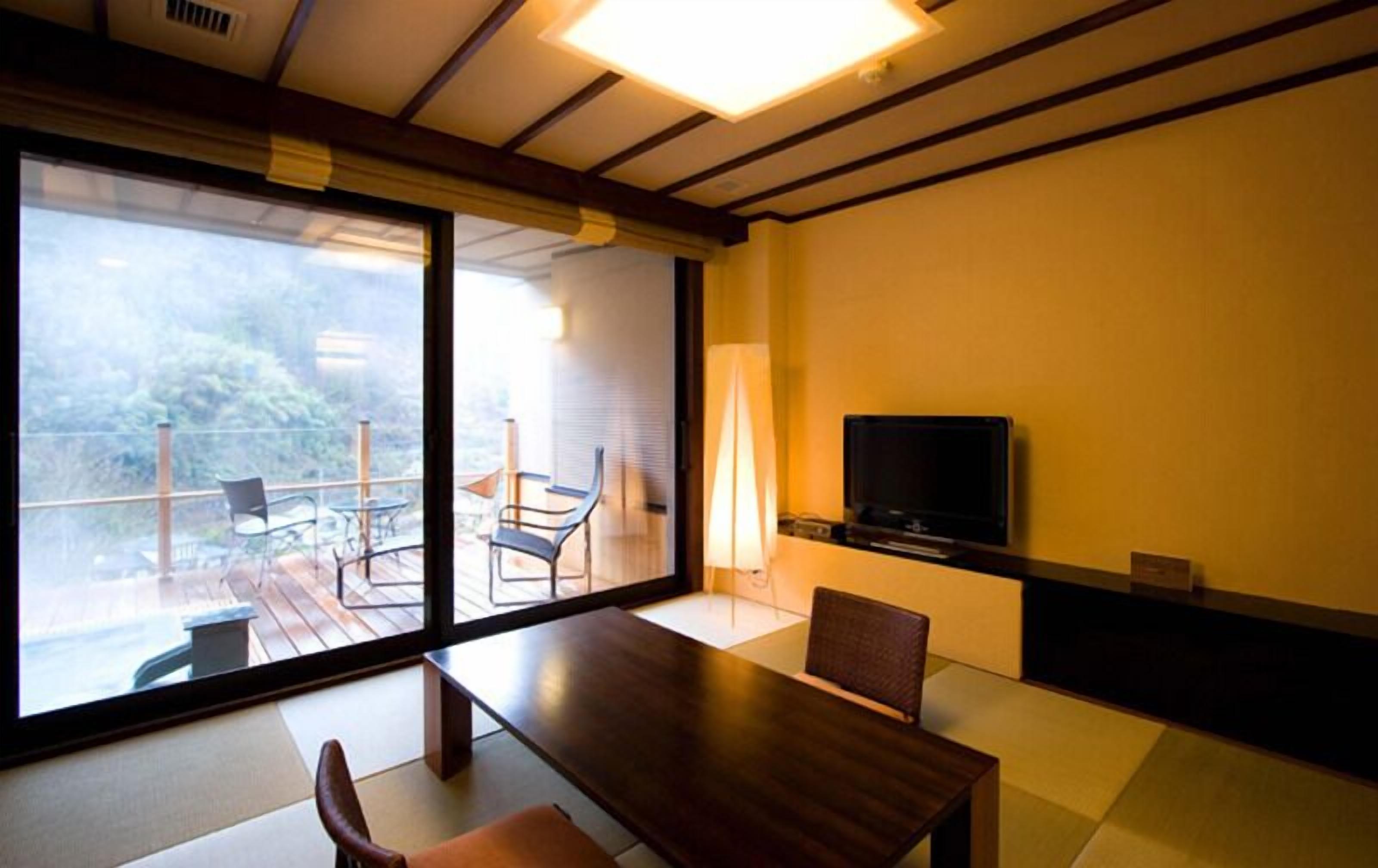 Ein modernes Zimmer mit einer großen Glasschiebetür, die auf eine Terrasse im Freien führt, einem Holzesstisch und einem an der Wand befestigten Flachbildfernseher.