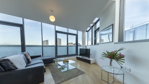 Una sala de estar moderna con un sofá, una mesa de centro de vidrio, un televisor y vista al mar.