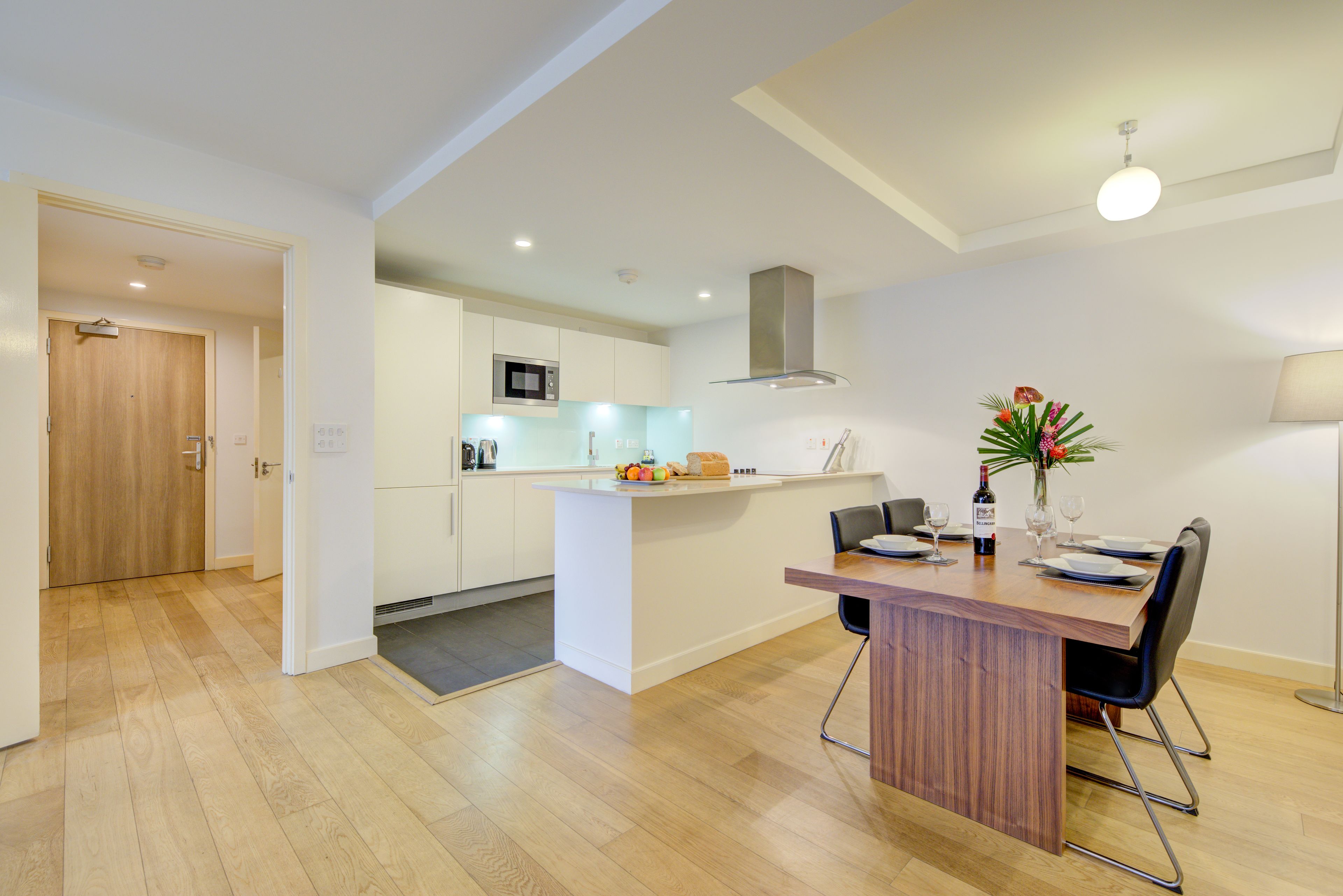 Uma cozinha moderna com armários brancos, uma ilha central e um espaço de refeições com mesa e cadeiras de madeira.