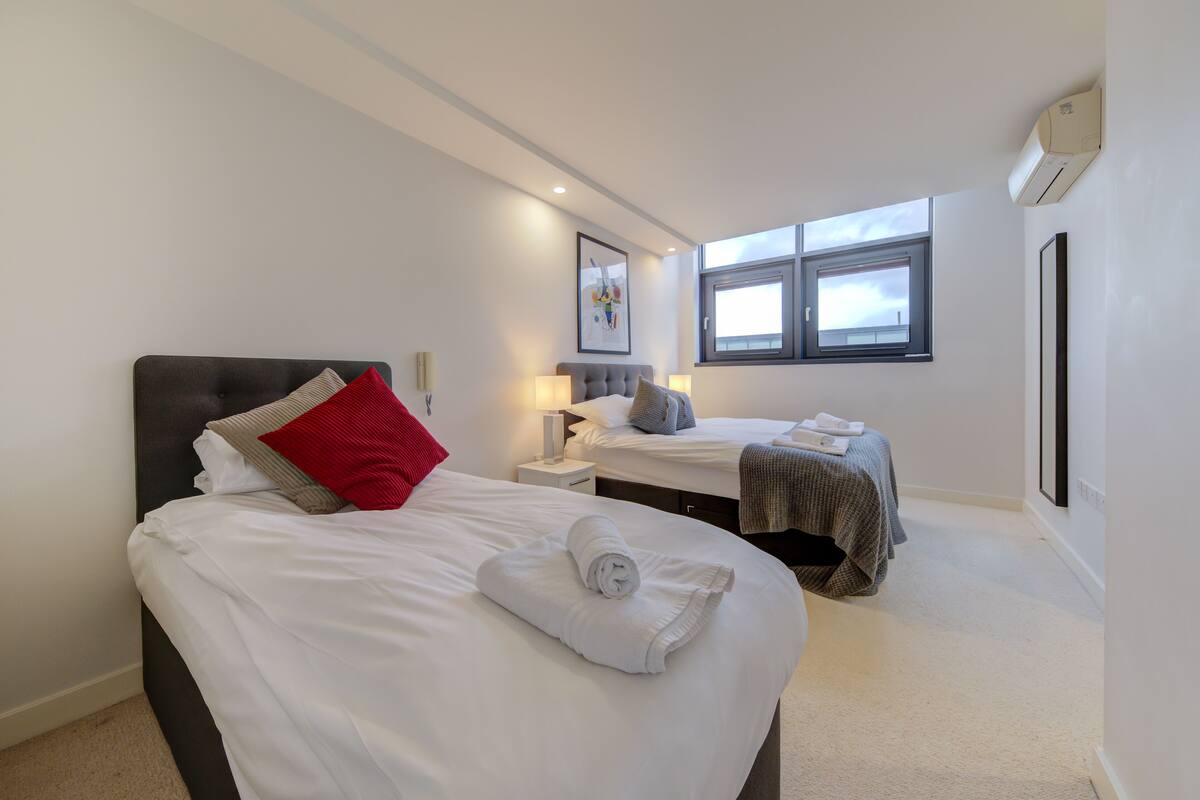 A hotel room with two beds, a large window, and an air conditioning unit.