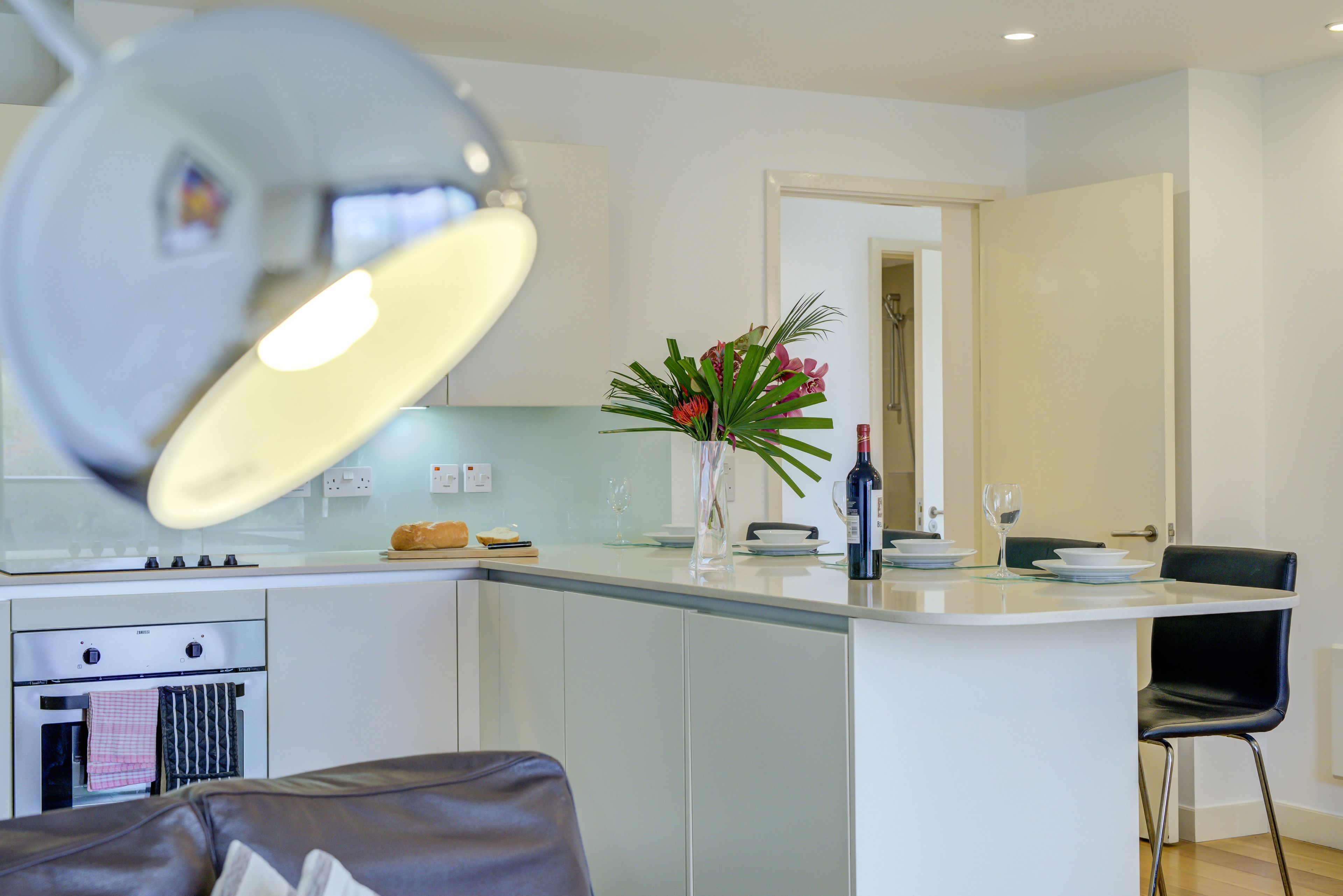 A modern kitchen with a central island, a dining area with a chair, and a visible oven.