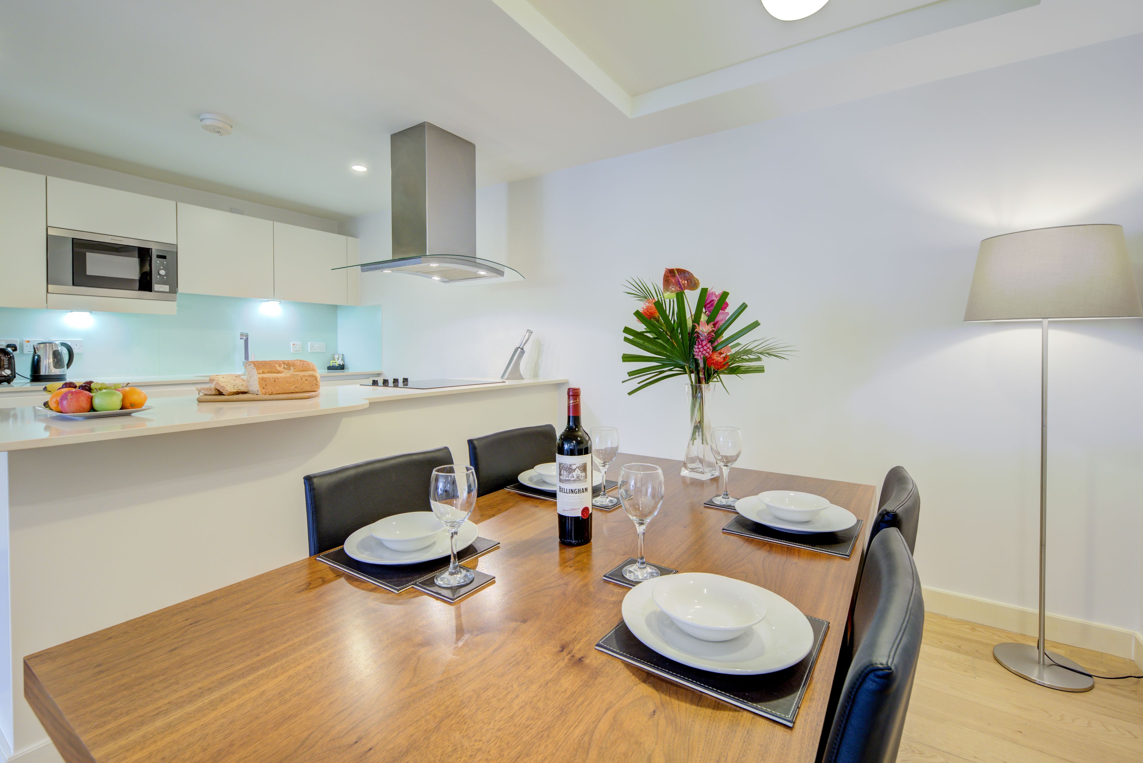 A dining area with a wooden table set for four, a bottle of wine, and a vase with flowers.