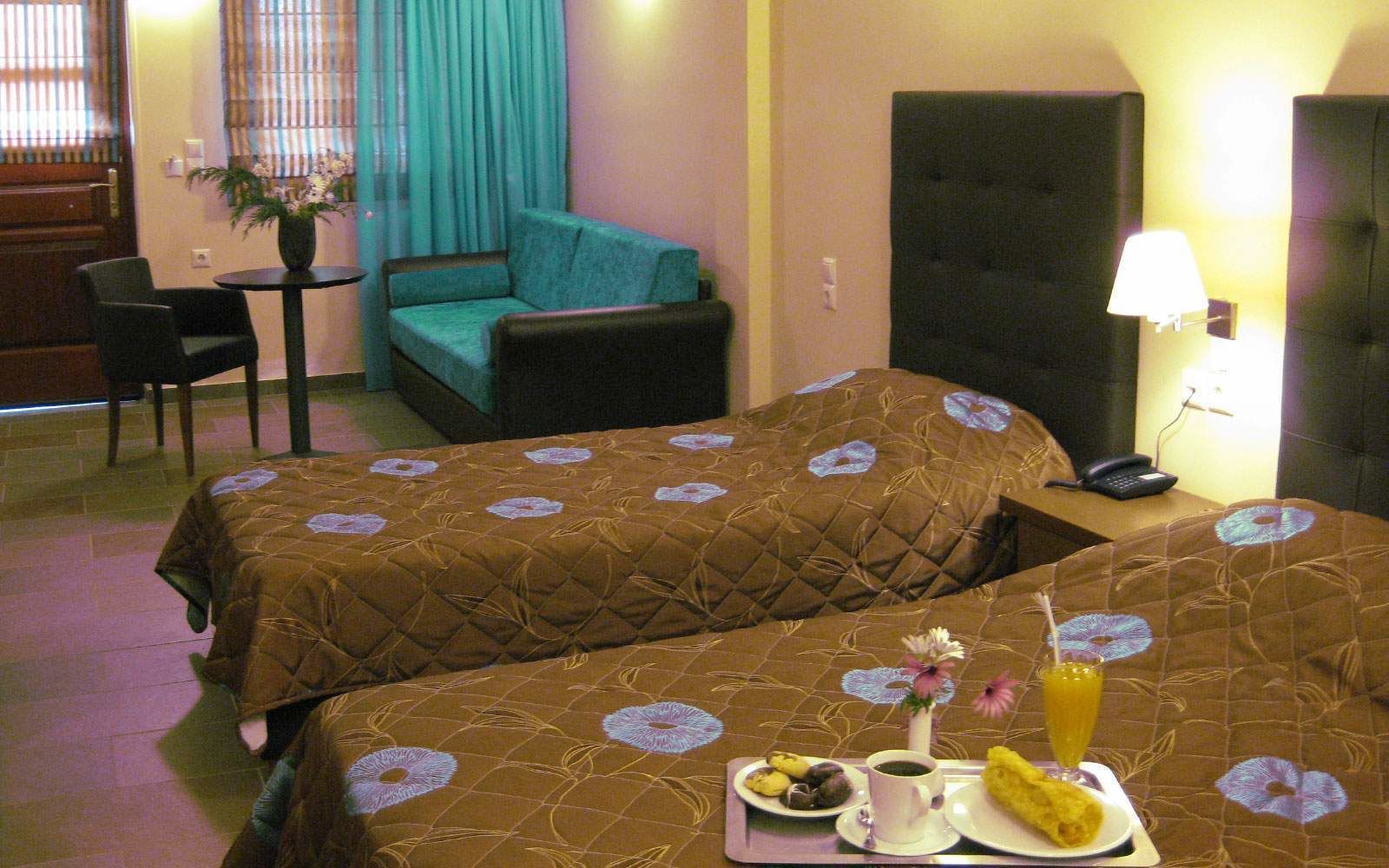 A hotel room with two beds, a small table with breakfast, a chair, a sofa, and a TV.