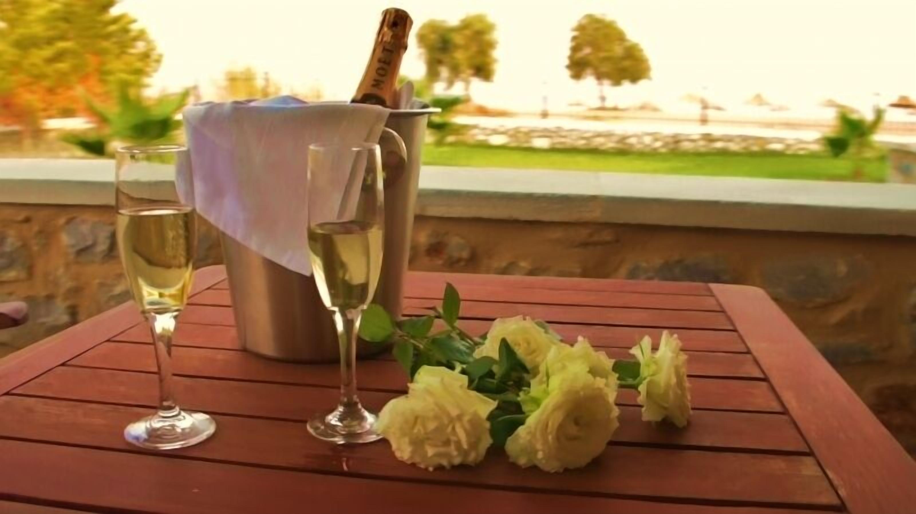 A table with two glasses of white wine, a champagne flute, and a bouquet of white flowers.