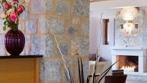 Una pared de piedra, un mostrador de recepción de madera, un jarrón con flores, una composición de velas y una chimenea al fondo.