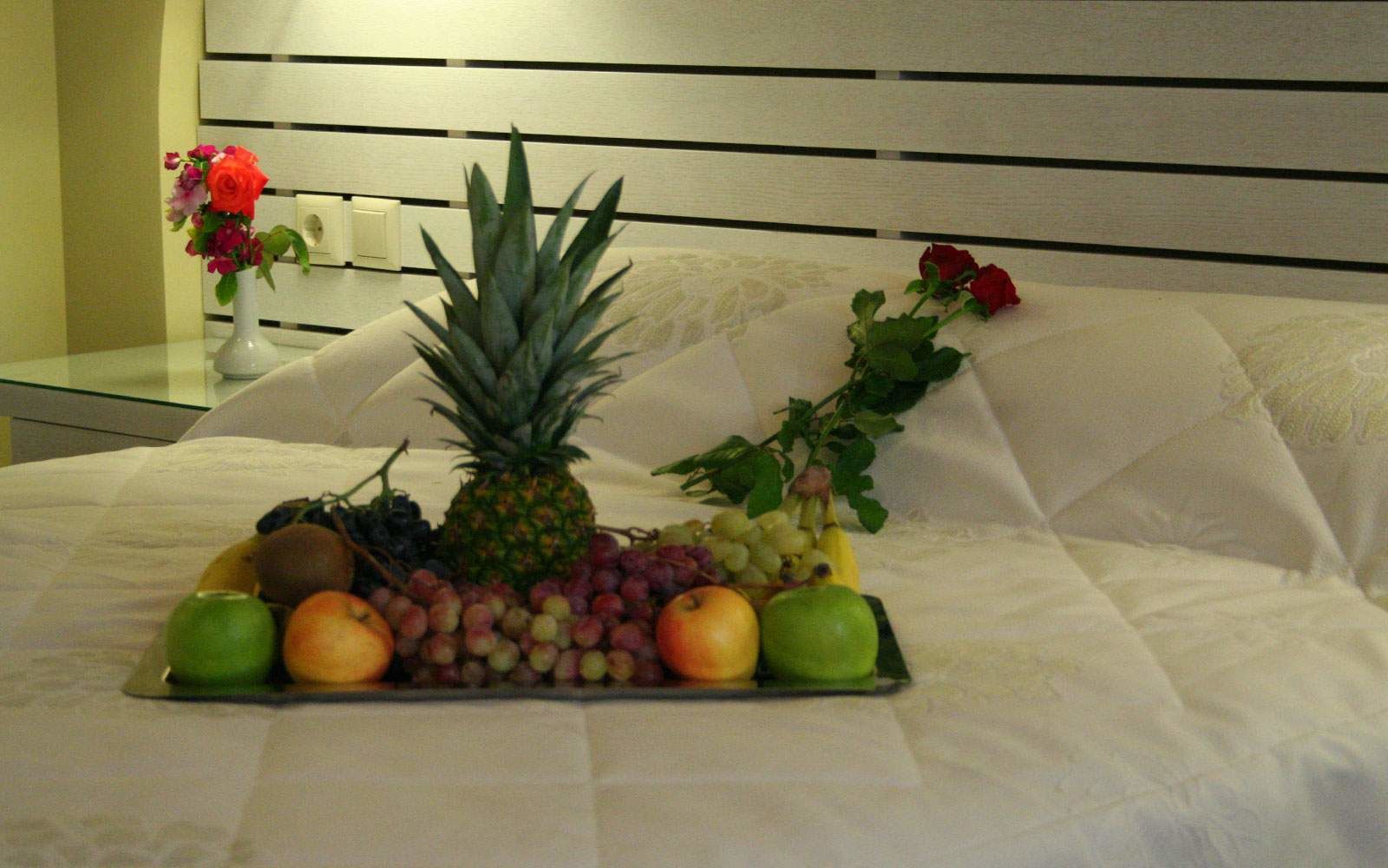 A bed with a fruit and flower arrangement on the side.