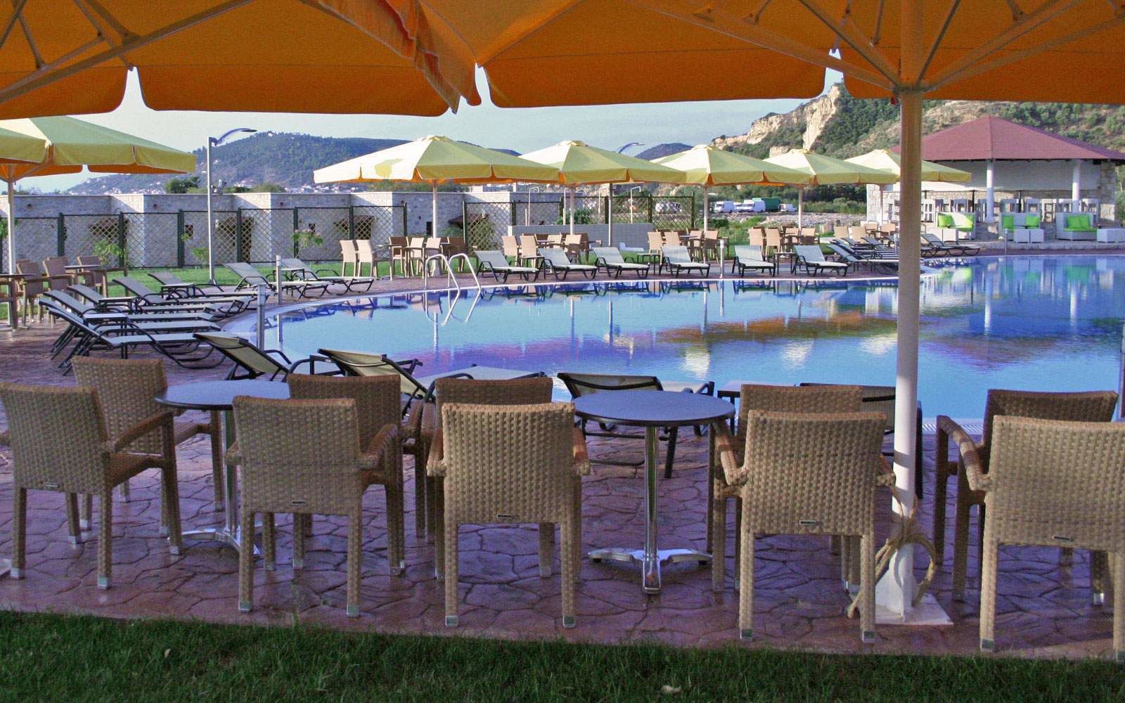 Un espace aménagé au bord de la piscine, avec des chaises longues et des parasols, une piscine, et un paysage montagneux en arrière-plan.
