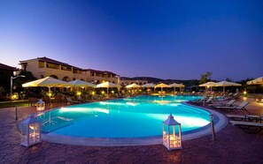 A large outdoor swimming pool with lounge chairs and umbrellas, surrounded by a building with multiple balconies.