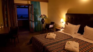 Habitación de hotel con cama, escritorio, silla, mesa con un florero y vista al océano.