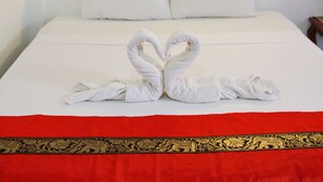 A hotel room with a bed, two pillows, a red bedspread, and a wall-mounted fan. - JJ Guesthouse (Karon)