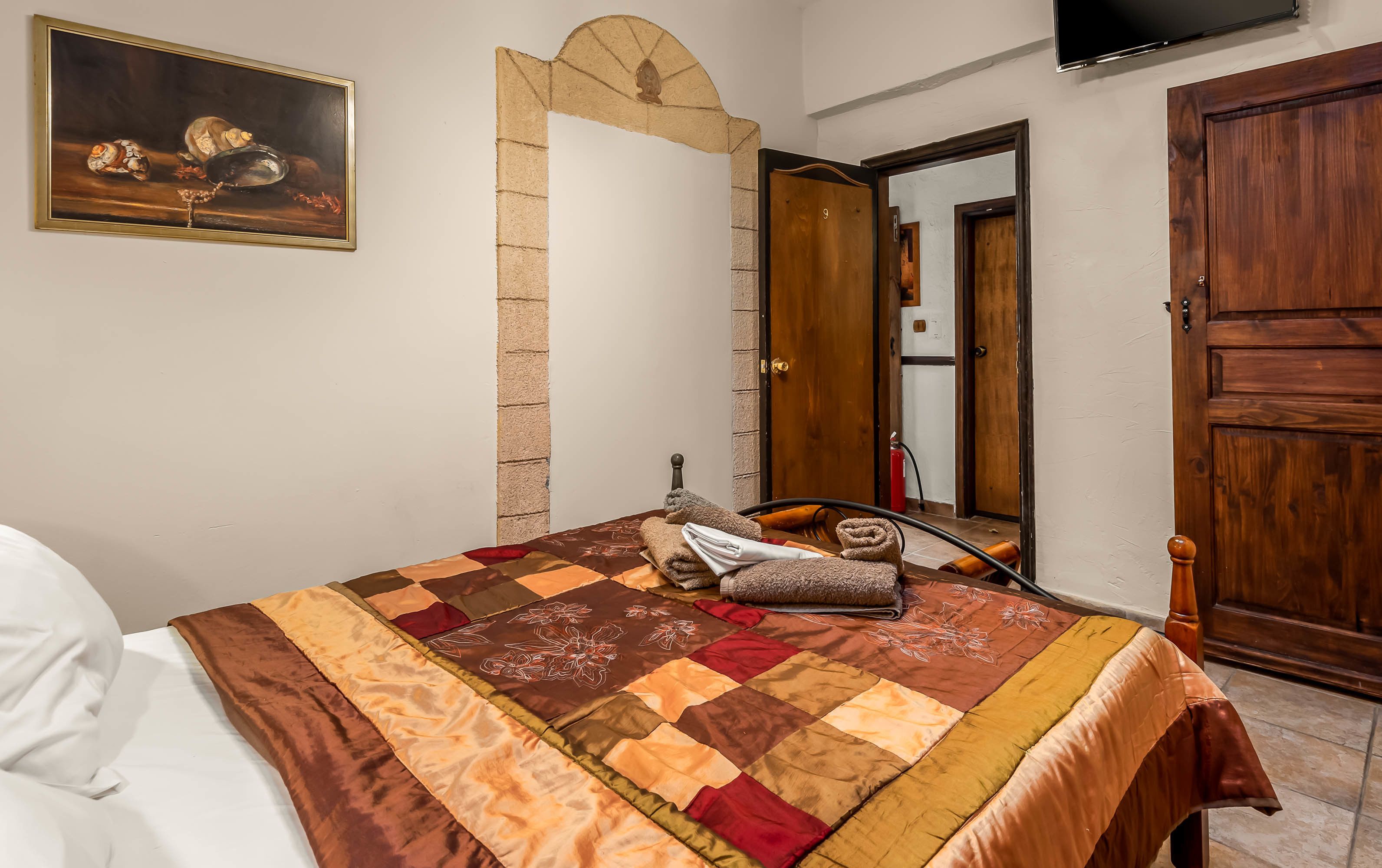 A bedroom with a bed, a painting, a wooden door, and a tiled floor.