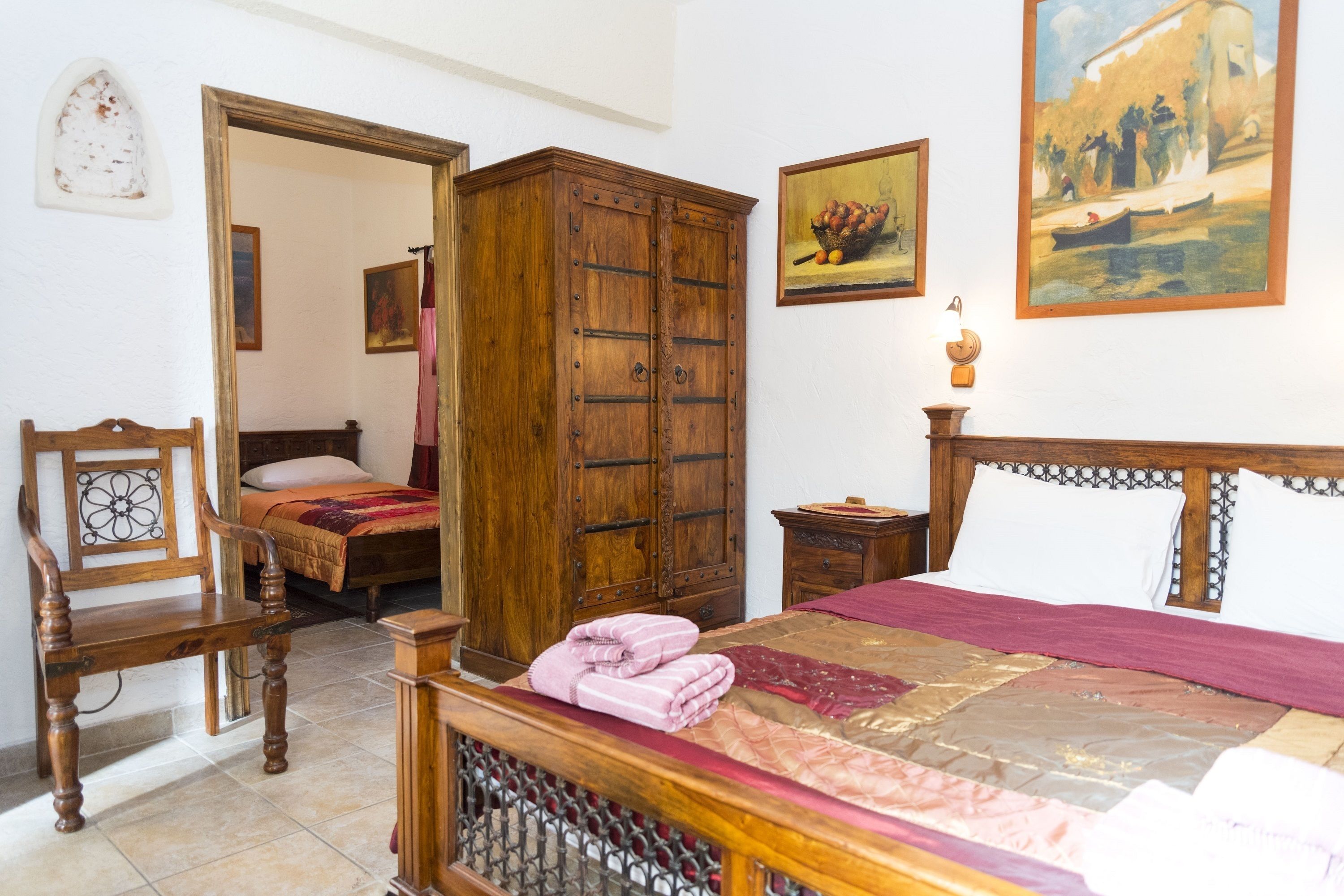 Un dormitorio con cama, armario y silla de madera, además de una mesita de noche con lámpara.