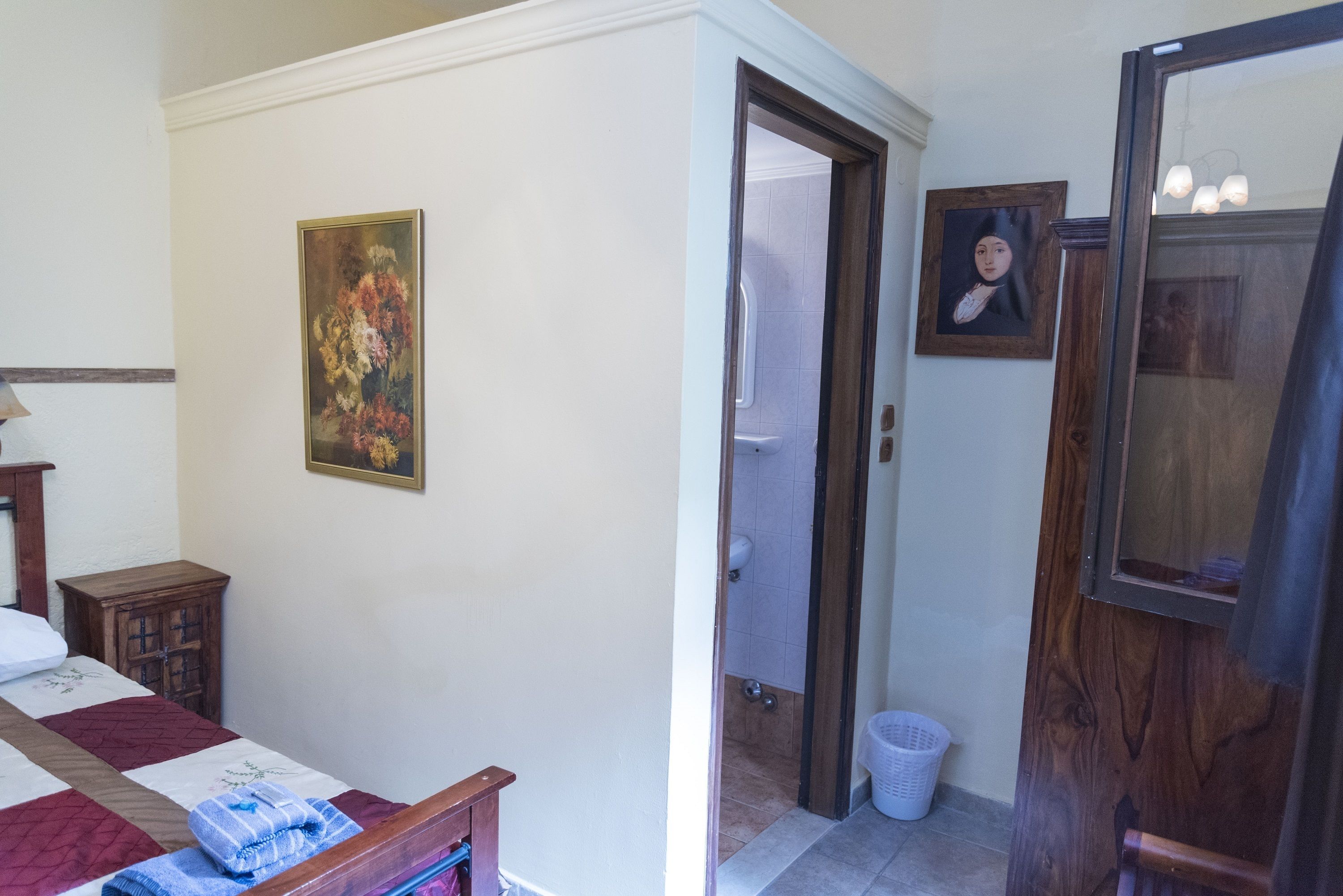 Un dormitorio con una cama, un armario de madera, un cuadro y una puerta que da al baño.