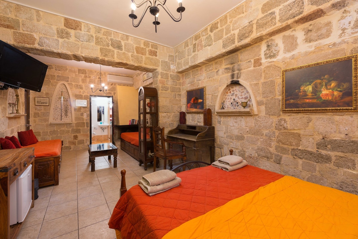 Habitación con paredes de piedra, una cama, un escritorio y un televisor.