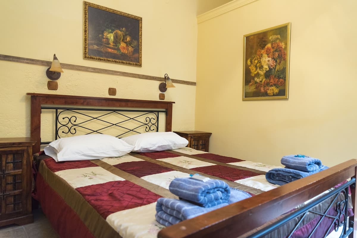 Una cama bien hecha con un colcha roja y blanca, dos almohadas y toallas dobladas sobre un cabecero de madera.