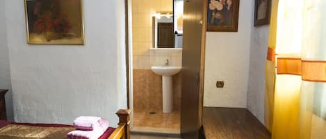 A hotel room with a bed, a wooden bench, a sink, and a door leading to a bathroom.