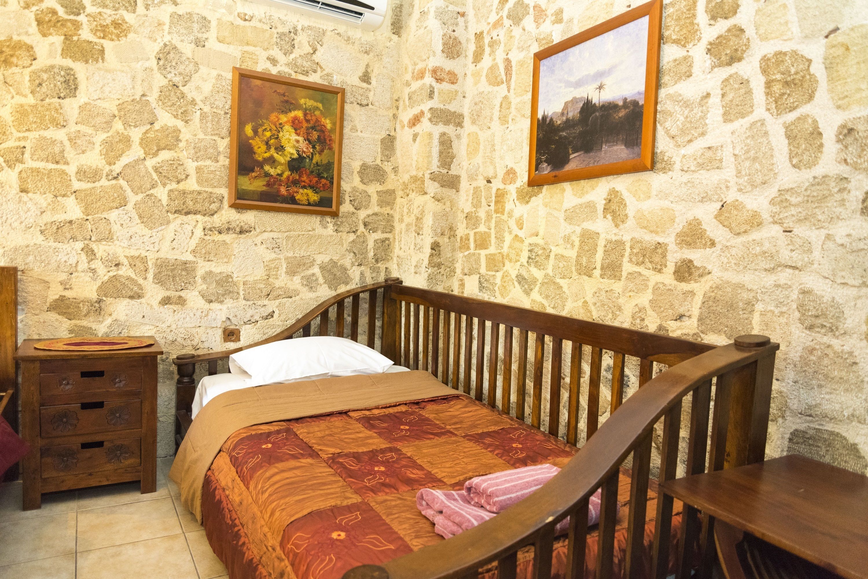 A bedroom with a stone wall, a wooden bed, a nightstand, and a framed picture on the wall.