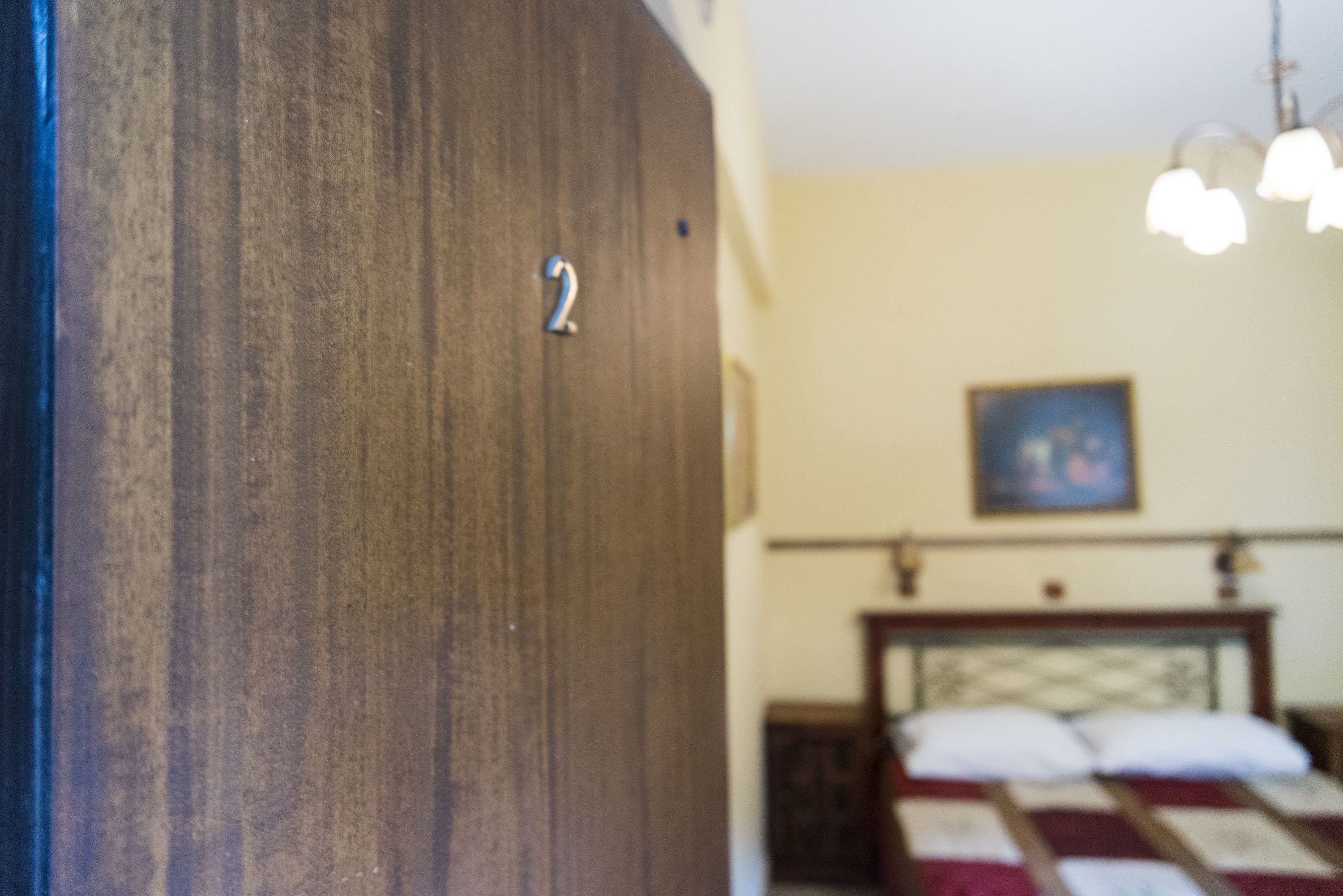 Une porte en bois portant le numéro « 2 », un lit avec une couverture et un tableau accroché au mur.