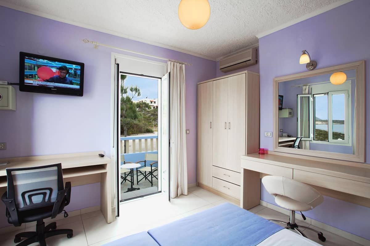 Ein Schlafzimmer mit Bett, Schreibtisch, Stuhl, Fernseher, Kleiderschrank und einem Balkon mit Meerblick.