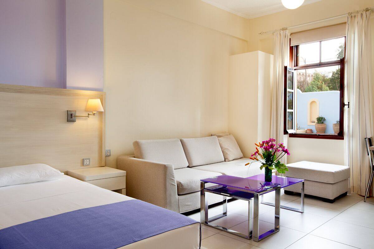 Ein Hotelzimmer mit Bett, Sofa, einem kleinen Tisch mit Blumenvase und einem Fenster mit Vorhängen.