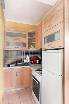 Eine kleine Küche mit Holzausstattung, einem weißen Kühlschrank, einem Herd und einer gefliesten Spritzschutzwand.