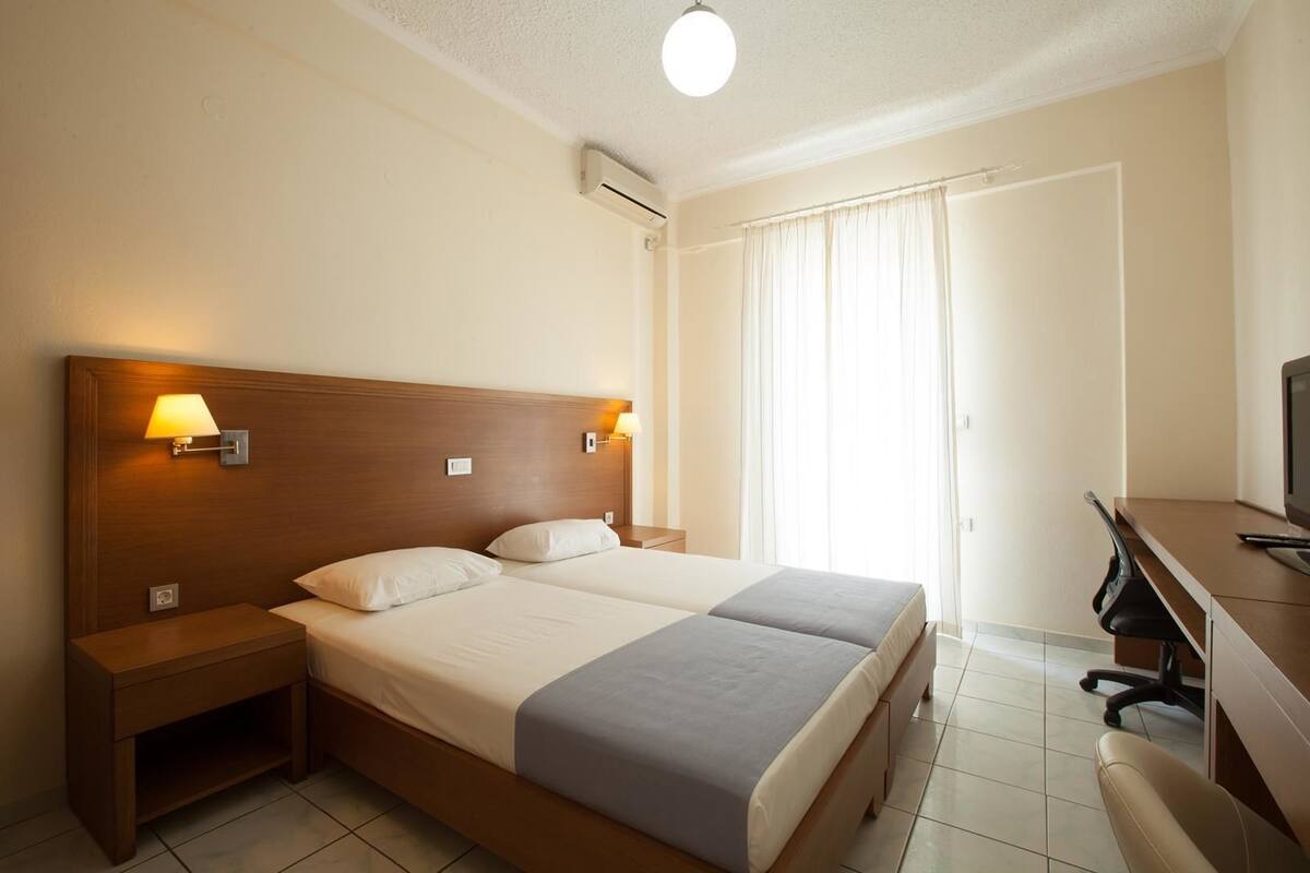 Ein Hotelzimmer mit zwei Betten, einem Schreibtisch mit Stuhl und einem Fernseher.