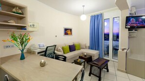 En moderne stue med sofa, spisebord, TV og en balkon med gardiner.