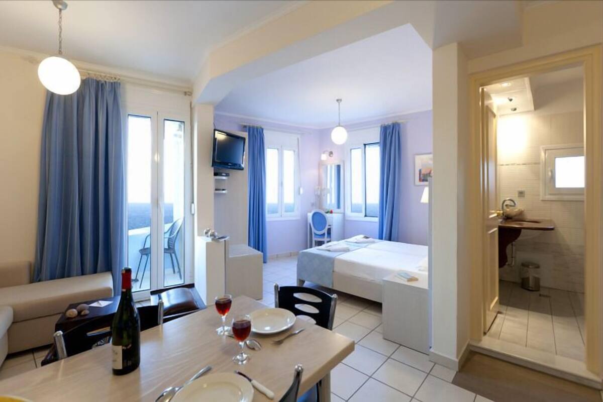 Ein Hotelzimmer mit Essbereich, einem Bett, einem Fernseher und einem Badezimmer.