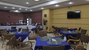 Una sala de conferències amb taules i cadires, un ventilador al sostre i una televisió penjada.