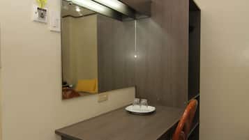 Quarto pequeno e moderno com escrivaninha de madeira, uma cadeira, um espelho e um prato com dois copos na escrivaninha.