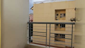 Un balcón con barandilla metálica, una puerta con pomo redondo y un edificio color beige con una ventana y una puerta pequeña al fondo.