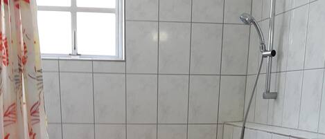 A bathroom with a shower, toilet, and a window.