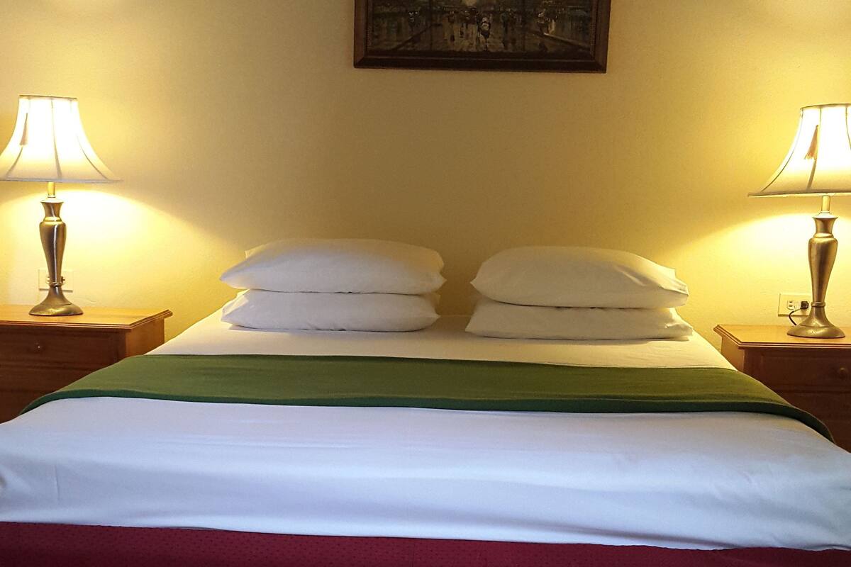 A hotel room with a bed, two bedside lamps, a painting on the wall, and a tiled floor.