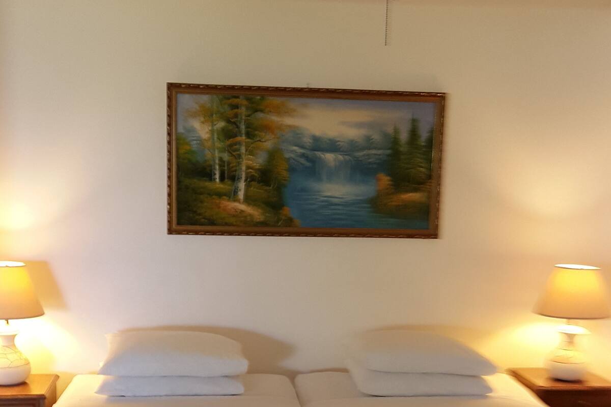 A bedroom with two beds, a ceiling fan, a painting, and two bedside lamps.