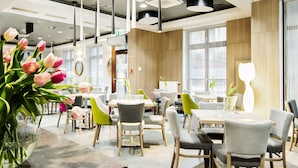 A modern dining area with wooden tables, grey and green chairs, and a vase of pink tulips.