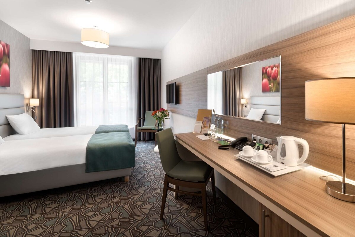Une chambre d’hôtel équipée d’un lit, d’un bureau, d’une chaise, d’une machine à café et d’un miroir.