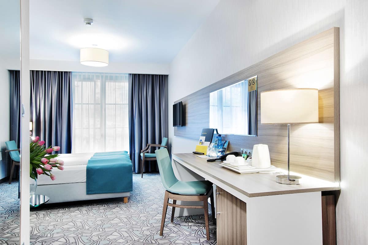 Une chambre d’hôtel moderne équipée d’un lit, d’un bureau, d’une chaise, d’une télévision et d’une lampe.