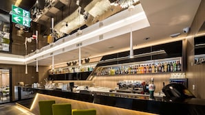 Un'area bar moderna con un lungo bancone, diversi sgabelli da bar e una varietà di bottiglie di liquore.