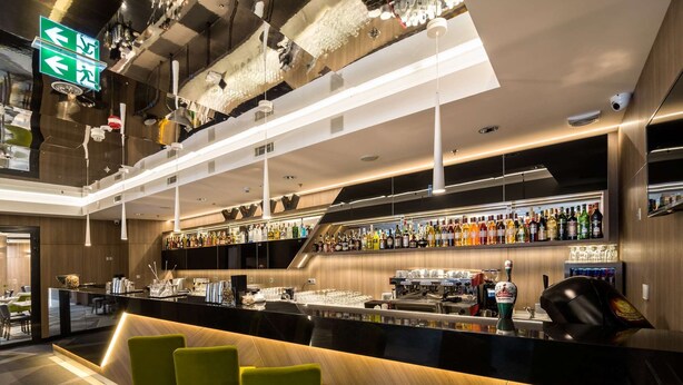 A modern bar area with a long counter, multiple bar stools, and a variety of liquor bottles.