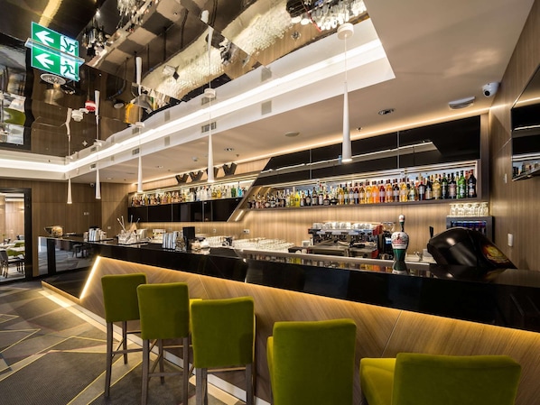 Een moderne bar met een lange toonbank, diverse barkrukken en een selectie drankflessen.