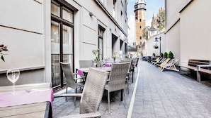 An outdoor dining area with wicker chairs and tables, a wine glass, and a view of a historic tower in the background.