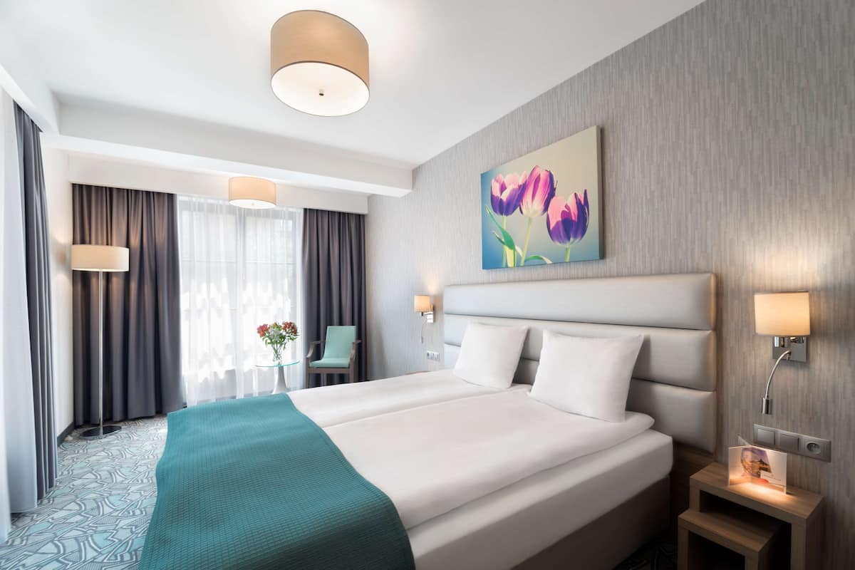 Une chambre d’hôtel avec un grand lit, une table de chevet avec une lampe, une petite table avec un vase et un tableau au mur.